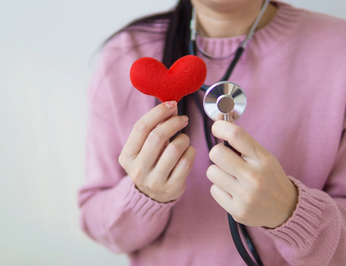 person holding a heart while wearing a stethoscope